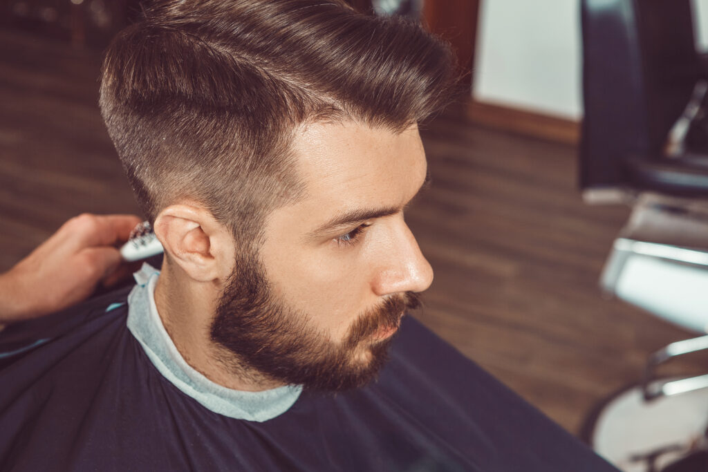 The hands of young barber making haircut to attractive man in barbershop